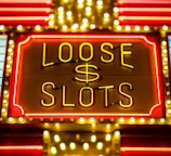 Bright neon lights display the words 'Loose Slots' with a dollar sign in the center. The sign is outlined with bulbs, creating a vibrant and flashy effect typical of a casino or entertainment venue.