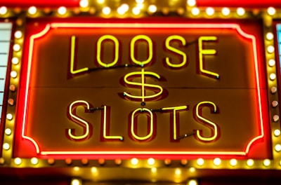 Bright neon lights display the words 'Loose Slots' with a dollar sign in the center. The sign is outlined with bulbs, creating a vibrant and flashy effect typical of a casino or entertainment venue.